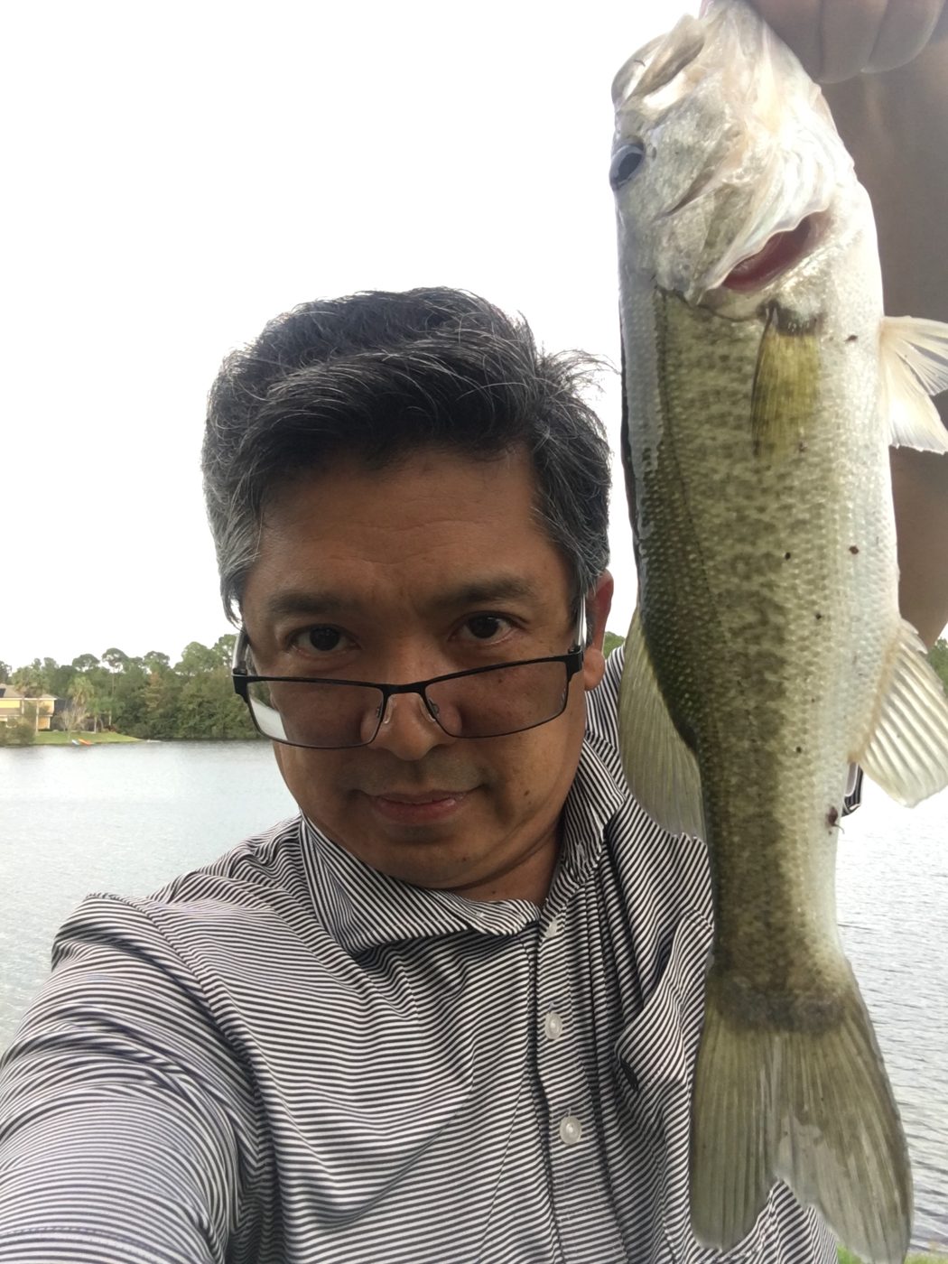 Renato Cruz Sogueco holding a largemouth bass by a lake
